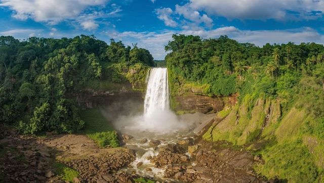 Plunging tropical waterfall creating mist over rocky gorge with lush canopy