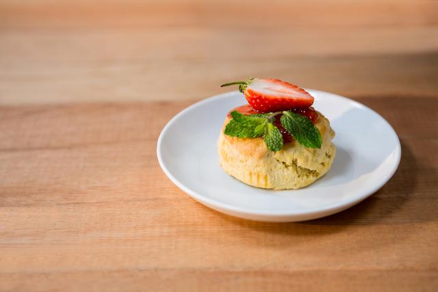 This image features a close-up of a strawberry shortcake garnished with fresh mint leaves, placed on a white plate on a wooden table. Ideal for use in food blogs, recipe websites, culinary magazines, or advertisements for bakeries and dessert shops.