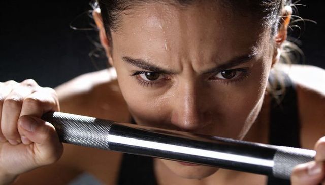 Female athlete gripping knurled bar under chin, sweat glistening, intense focus