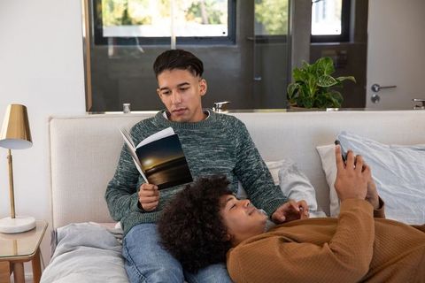 Couple Sharing Relaxing Moments with Book and Smartphone in Cozy Bedroom