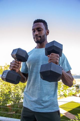 Man Lifting Dumbbells on Balcony Under Blue Sky