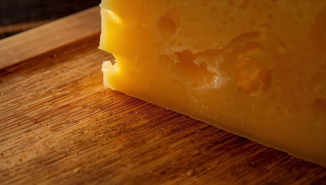 Rustic swiss cheese wedge resting on wooden cutting board showing holes, crumbs and rich texture