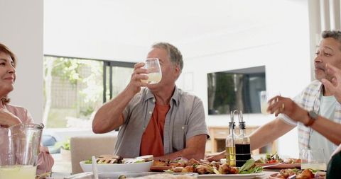 Sunlit casual brunch gathering with man raising glass and friends sharing salad