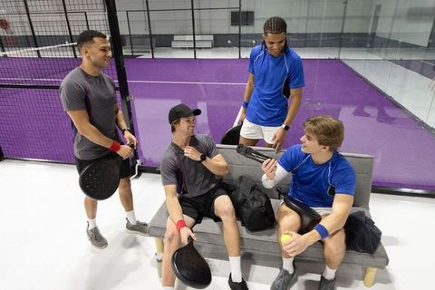After-match camaraderie on purple padel court male teammates relaxing with paddles