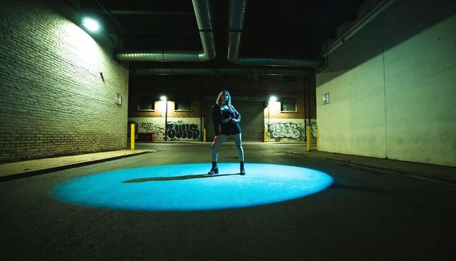 Woman posing under blue spotlight in urban alley at night for edgy street fashion