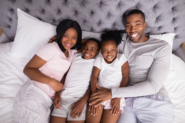 Family of four lying on bed, smiling and enjoying time together. Perfect for use in advertisements, family-oriented content, lifestyle blogs, and articles about family bonding and home life.