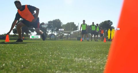 Male Soccer Player Lunging for Cone During Agility Drill on Sunlit Turf with Team
