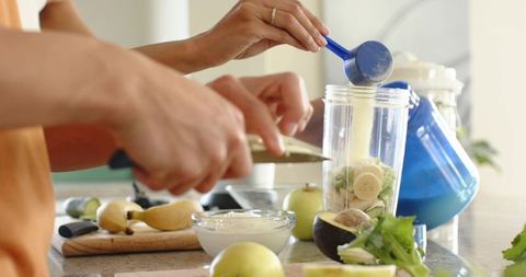 Couple making green smoothie pouring supplement and slicing bananas on kitchen counter