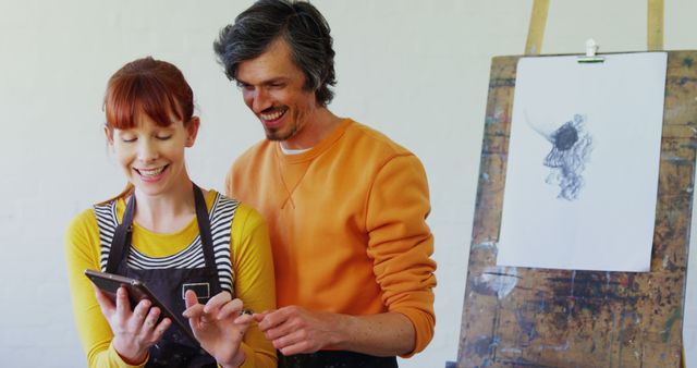 Two artists are discussing artworks happily in a studio, highlighting their friendly and collaborative dynamic. The background shows an easel with a sketch, indicating an inspiring creative environment. Ideal for depicting collaboration in the creative industry, artistic consultations, or promoting art workshops and classes.
