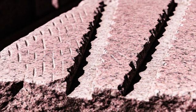 Sunlit pink granite slab with three parallel chisel grooves and rugged texture