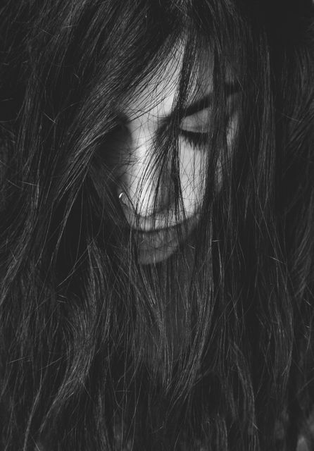 Close-up of a woman with long, messy hair partially covering her face, captured in high contrast black and white. Perfect for conveying emotions like sadness, introspection, and moodiness. Can be used for artistic projects, mental health awareness campaigns, or emotional expression themes.