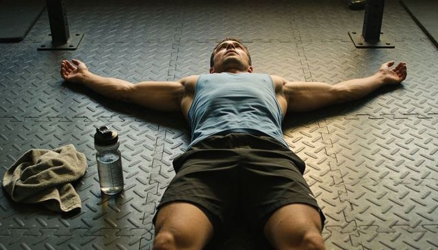 Exhausted athlete lying on gym floor after intense workout recovering and hydrating