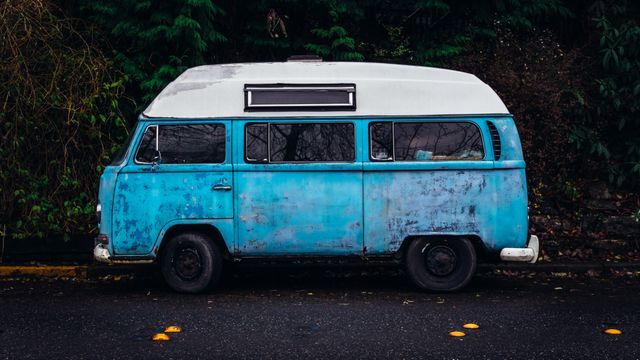 This photo captures a rustic, blue camper van parked alongside a road with lush greenery in the background. The setting evokes a sense of nostalgia and adventure, suggesting road trips, travel, and exploration. Suitable for travel blogs, vintage vehicle enthusiasts, adventure-themed marketing, and nature-related content.