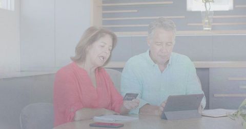 Senior couple using tablet and credit card at kitchen table managing online finances