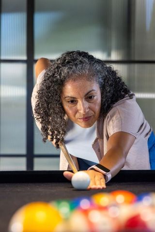 Senior african american woman lining up cue shot at pool table, concentrating in daylight
