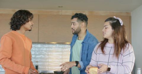 Friends chatting in modern kitchen showing smartwatches and holding breakfast bun