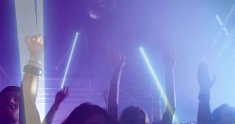 Crowd raising glow sticks and cheering in neon-lit nightclub with fog and led tubes