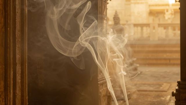 Incense smoke drifting through temple entrance framing carved pillar in warm sunlight