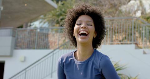 Sunlit african american woman laughing on modern patio conveying joyful lifestyle energy