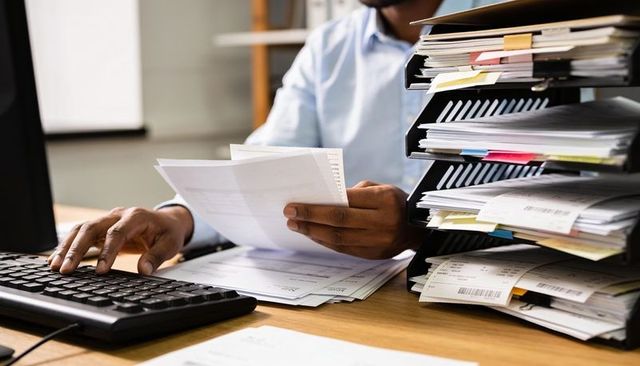 Hands reviewing documents and typing at busy office desk with stacked file organizer