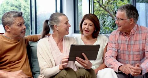 Diverse Senior Friends Discussing Over Tablet at Home