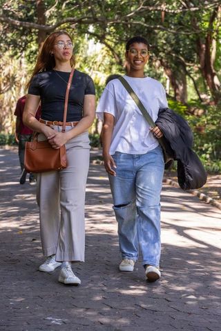 African american friends walking on tree-lined park path, casual style, smiling