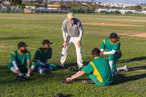 Amateur baseball team stretching on grass with coach leading warm-up and team talk