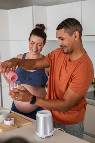 Pregnant couple making smoothie in modern kitchen