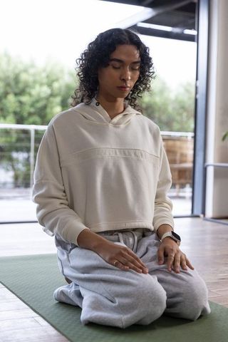 Non-binary person practicing mindful kneeling meditation on green yoga mat in sunlit home