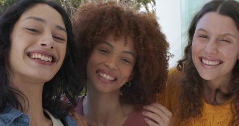 Diverse women leaning and smiling together on porch touching shoulders, casual happy trio
