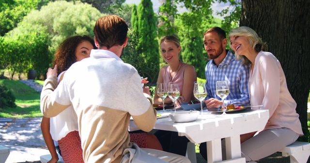 Group of friends enjoying meal together in park, surrounded by trees and natural scenery. Perfect for promoting social events, outdoor activities, friendships, and summer gatherings.