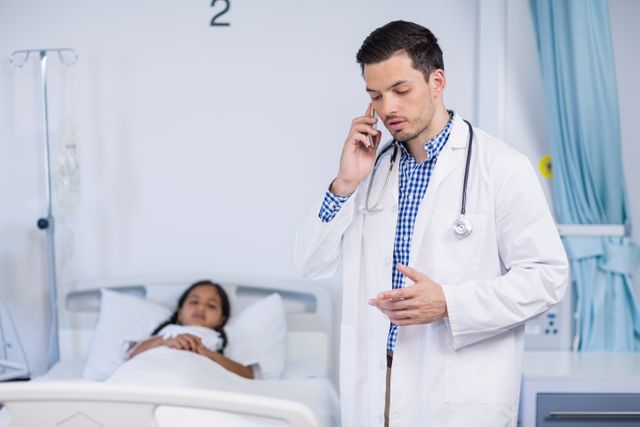 Doctor talking on mobile phone in hospital room with patient lying in bed. Useful for illustrating healthcare communication, medical consultations, hospital environments, and professional healthcare services.