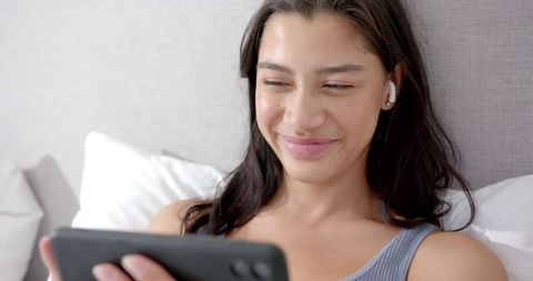 Teenager Relaxing on Bed While watching Smartphone with Earphones