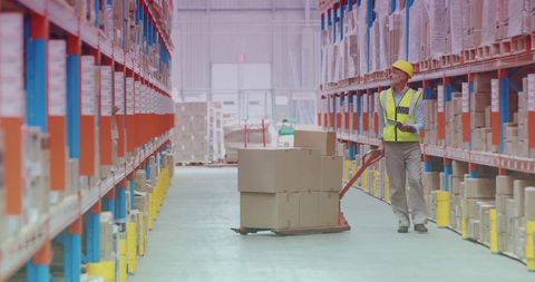Warehouse worker scanning inventory with tablet and pallet jack in high-bay racking aisle