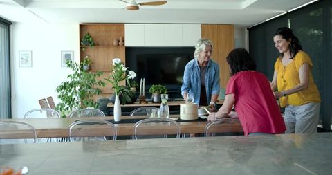 Diverse women arranging table for casual indoor gathering, modern plant-filled dining room