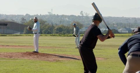 Amateur baseball pitcher preparing throw while batter readies swing on sunny local diamond
