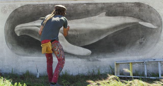 Street artist painting a large monochromatic whale mural on an outdoor wall. Ideal for themes related to urban art, creativity, public murals, marine life awareness, and outdoor artwork. Useful in projects promoting street art, wildlife conservation, and community beauty through public art installations.