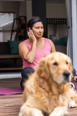 Mature woman practicing yoga on deck with golden retriever companion for home wellness