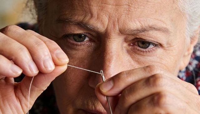Senior woman threading needle with steady fingertips closeup for sewing and crafts