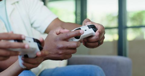 African american father and teen son playing video games on couch sharing joyful bonding