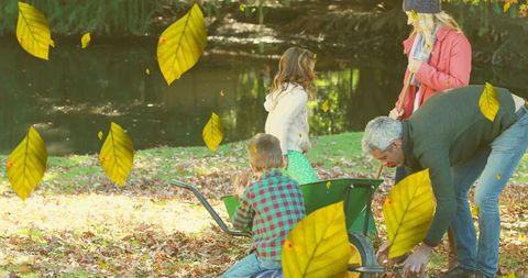 Family fun raking leaves by pond in autumn