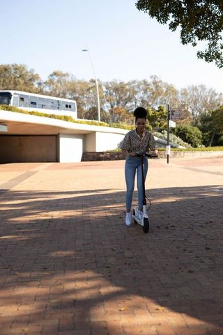 Woman riding electric scooter on sunny urban plaza