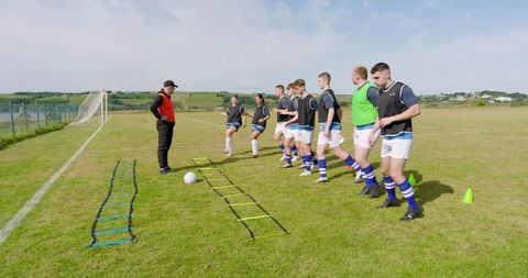 Coach leading youth soccer team in ladder drills on grassy field