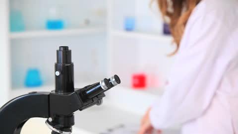 Female Scientist Observing Samples with Microscope in Modern Laboratory