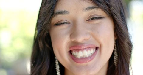 Sunlit closeup smiling young woman showing teeth wearing long beaded dangling earrings
