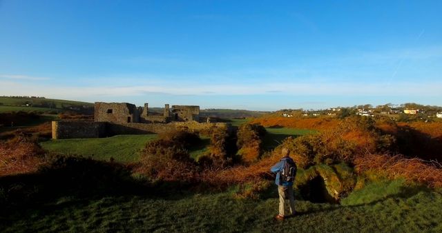 Traveler in weathered clothing explores old ruins in hilly countryside under clear blue sky. Ideal for outdoor adventure concepts, historical exploration themes, travel promotion, and nature appreciation campaigns.