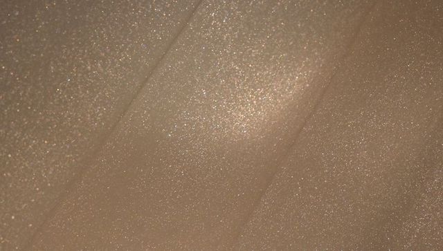 Shimmering beige tulle with fine glitter and soft diagonal folds for luxury textile designs