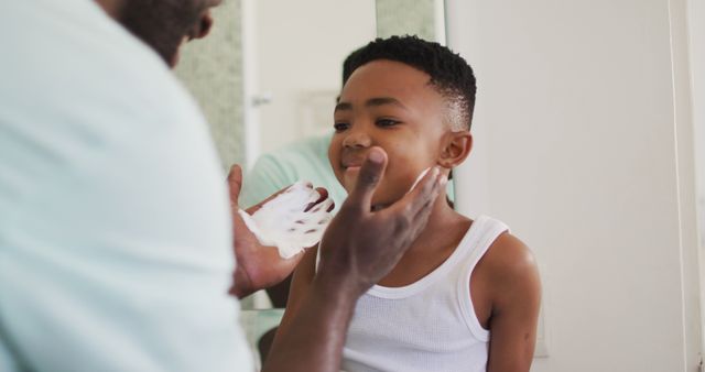 African american father putting shaving cream on his son mouth and laughing together. staying at home in self isolation during quarantine lockdown.