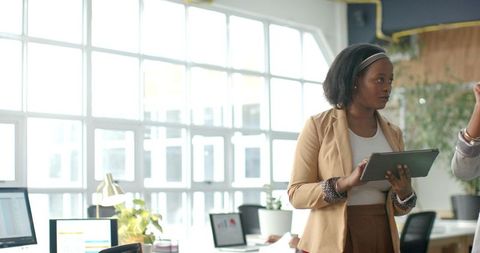 African American professional holding tablet collaborating in bright open office