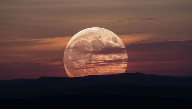 Giant full moon rising over layered mountain ridges at twilight with dramatic orange sky